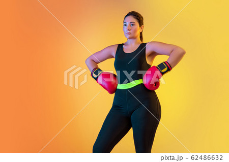 Young caucasian plus size female model's training on gradient orange background 62486632