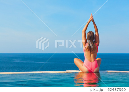 Woman at edge of infinity swimming pool with sea 62487390