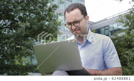 Comic emotion. Young businessman with disgusted emotion holding laptop in a park. 62488861
