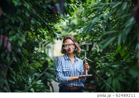 Young woman with windmill model standing in botanical garden. Young woman with windmill model standing in botanical garden. 62489211