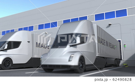 Modern semi-trailer trucks with MADE IN IRELAND text being loaded or unloaded at warehouse. Turkish business related 3D rendering 62490828