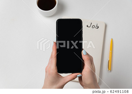 Female hand holding mobile phone. Notepad and cup Female hand holding mobile phone. Notepad and cup 62491108