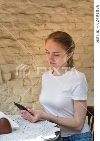 Girl sits at table and holds the phone. Student, 62491886