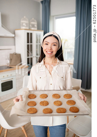 Woman with baking tray standing at home. 62501773