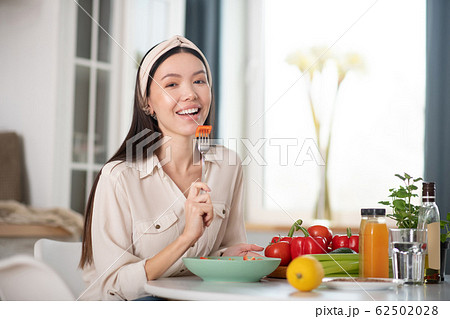 Happy young woman sitting at a table with a fork. Happy young woman sitting at a table with a fork. 62502028