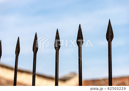 Wrought iron fence with sharp points on blue sky with clouds 62503229
