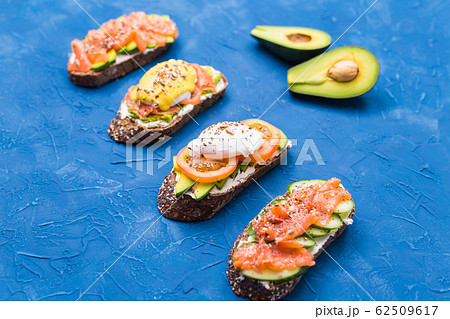 Sandwiches with smoked salmon, eggs, sauce and avocado on blue background. Concept of breakfast and healthy nutrition. Sandwiches with smoked salmon, eggs, sauce and avocado on blue background. Concept of breakfast and healthy nutrition. 62509617