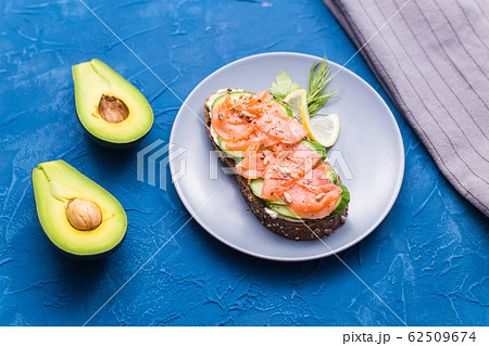 Sandwich with smoked salmon and cucumber on blue background with avocado, top view. Concept for healthy nutrition. Sandwich with smoked salmon and cucumber on blue background with avocado, top view. Concept for healthy nutrition. 62509674