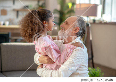 Grey-haired man and a dark-skinned girl looking at each other Grey-haired man and a dark-skinned girl looking at each other 62510580