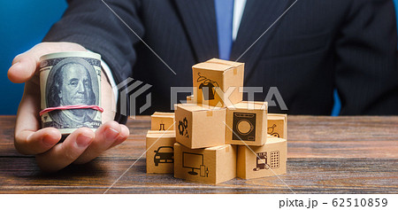 Businessman holds out a bundle of dollars near a pile of boxes. Profit, Superprofits. Investments financing in production, taxes, income revenues. Trade and exchange goods, offers for cooperation. 62510859