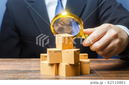 Businessman examines boxes goods with magnifying glass. Marketing sales promotion strategy. Trade market structure research, find unoccupied target consumer niches. Quality control and standards 62510861