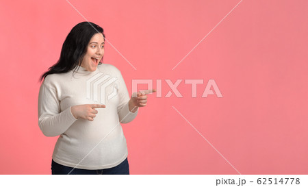 Surprised Plump Woman Pointing Aside At Copy Space On Pink Background 62514778