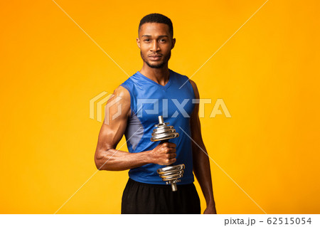 African bodybuilder pumping up biceps with dumbbells at gym 62515054