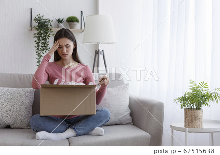 Negatively surprised girl sitting on coach and looking into cardboard box Negatively surprised girl sitting on coach and looking into cardboard box 62515638