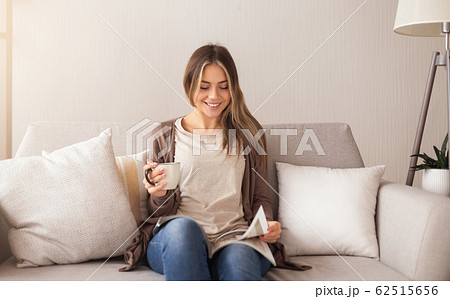 Smiling woman sitting on couch and reading magazine 62515656
