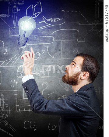 Businessman hand touches lightbulb over gray wall background. Businessman hand touches lightbulb over gray wall background. 62517748
