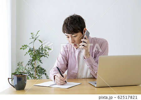 スマホで通話しながらメモをとる男性 62517821