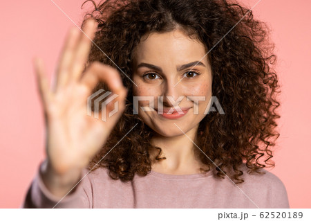 Winner. Success. Positive girl making OK sign over pink background and smiles to camera. Body language. Young curly woman with trendy glitter freckles make-up 62520189