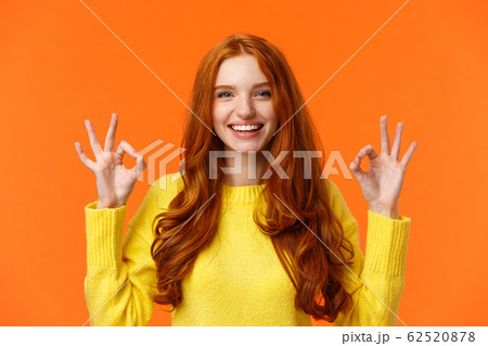 Fashion, shopping, winter holidays concept. Attractive cheerful redhead woman showing okay gestures and smiling, everything alright, approve or like product, recommend online store, orange background Fashion, shopping, winter holidays concept. Attractive cheerful redhead woman showing okay gestures and smiling, everything alright, approve or like product, recommend online store, orange background 62520878