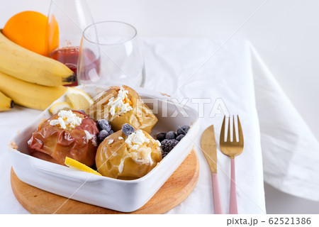 Baked apples with blueberries and cottage cheese in bowl with cutlery on white table Baked apples with blueberries and cottage cheese in bowl with cutlery on white table 62521386