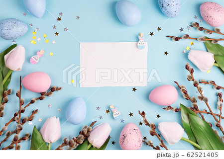 Easter willow wreath, white tulips and blue pink Easter eggs on blue background with sheet of paper. Top view, copy space Easter willow wreath, white tulips and blue pink Easter eggs on blue background with sheet of paper. Top view, copy space 62521405