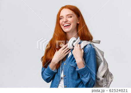 Charismatic and cheerful, lovely friendly redhead girl laughing over girlfriend joke as heading back campus from university classes, having fun chuckle with closed eyes, smiling, holding backpack 62524021