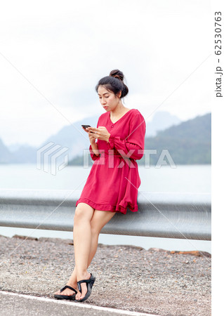 young asian woman sitting on guard rail and using 62530763