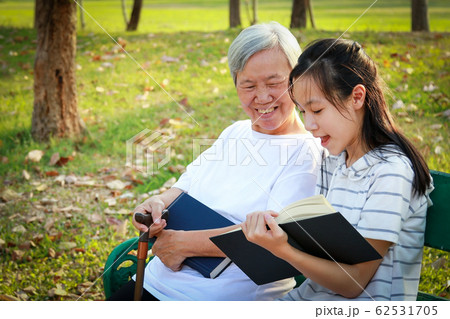 Happy asian granddaughter reading a book and senior grandmother together at summer park,loving child girl holding book sitting on bench having fun reading interesting book and telling story to elderly Happy asian granddaughter reading a book and senior grandmother together at summer park,loving child girl holding book sitting on bench having fun reading interesting book and telling story to elderly 62531705