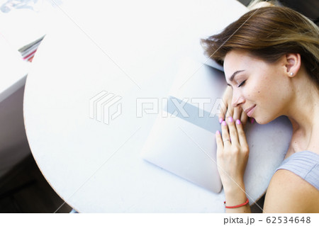 Blonde student lying on laptop at cafe in white background with copy space. 62534648