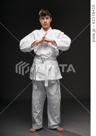 a teenager dressed in martial arts clothing poses on a dark gray background, a sports concept a teenager dressed in martial arts clothing poses on a dark gray background, a sports concept 62538410
