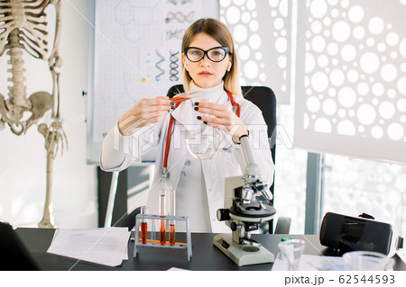 Pretty Caucasian woman researcher doctor chemist with glass equipment in the lab. Female professional scientist purifying red solution form tube into glass flask. Laboratory, clinical analysis concept 62544593