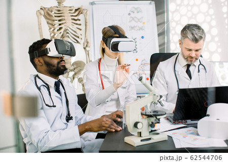 team of multiethnic scientists, African man, Caucasian woman and man, using virtual reality glasses for research in laboratory. Developmetn of new medicine, vaccine, substance 62544706