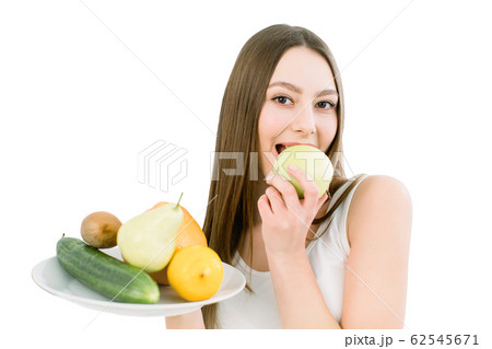 Woman holding fruits assortment served on white plate. Closeup portrait of cheerful young woman with perfect teeth biting green apple. Healthy, beauty concept. Isolated on a white background 62545671