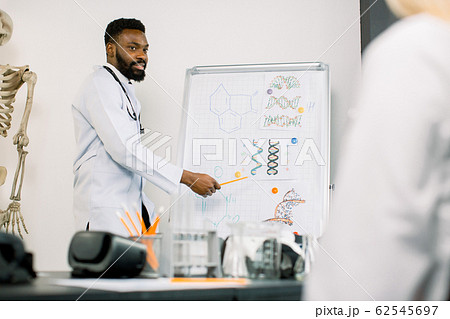 Portrait of young African male doctor or biochemist showing on board some biochemical formulas for his colleagues in conference room. Medicine, biochemistry, science concept 62545697
