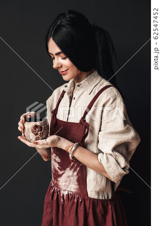 Craftsperson Concept. Young woman artist standing isolated on dark with cup smiling happy Craftsperson Concept. Young woman artist standing isolated on dark with cup smiling happy 62547452