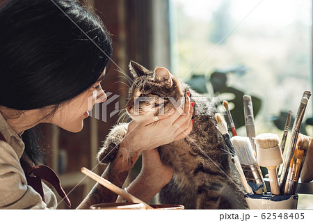 Craftsperson Concept. Young female artisit at creative studio sitting stroking cat smiling happy close-up 62548405