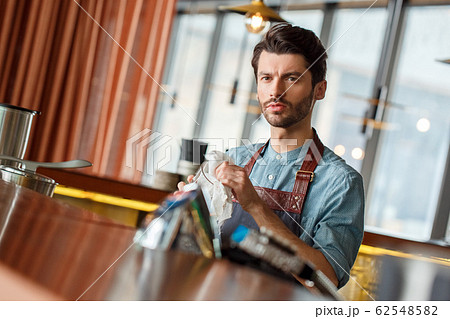 Professional Occupation. Bartender standing at counter wiping glass thoughtful 62548582