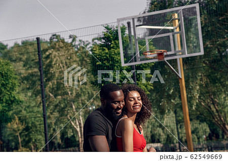 Outdoors Activity. African couple standing on basketball court hugging smiling joyful Outdoors Activity. African couple standing on basketball court hugging smiling joyful 62549669