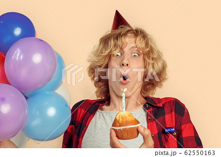 Young adult guy blowing on candle light at birthday cupcake 62550163