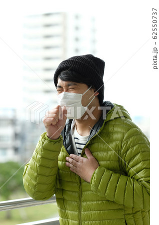 屋外で衛生マスクをして咳をしているニット帽をかぶった日本人男性のウエストアップ横顔 62550737