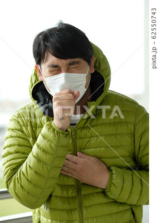 屋外で衛生マスクをして咳をしている日本人男性のウエストアップ正面 62550743