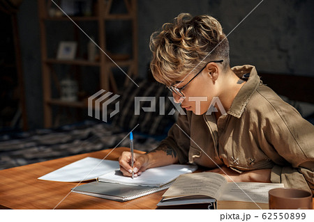 Education. Young woman short hair in glasses sitting at desk studying reading book taking notes concentrated close-up 62550899