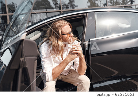 Young adult man sitting in car with open door and smoking Young adult man sitting in car with open door and smoking 62551653