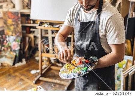 Male painter at art studio indoors mixing colors on palette with brush pensive working process close-up Male painter at art studio indoors mixing colors on palette with brush pensive working process close-up 62551847