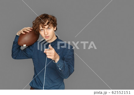 Sporty Lifestyle. Teenager boy standing isolated on grey with american football ball pointing at camera cool space for text or product 62552151