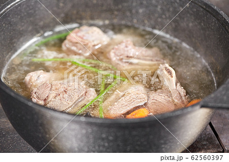 Traditional beef broth with vegetable, bones and ingredients in pot, cooking recipe. Soup in a cooking pot with ladle on dark stone background. Top view 62560397
