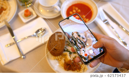 Hands using smartphone taking photos of chicken pasta with tomato coup and piece of bread 62573437