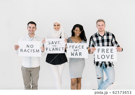Photo of four cheerful young multiracial friends posing isolated over white background, holding paper sheets with no racism, no war, save the planet text. The concept of peace on earth, equality 62573653