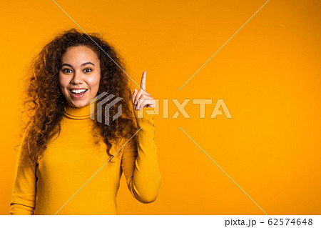 Portrait of young thinking pondering woman having idea moment pointing finger up on yellow studio background. Smiling happy girl showing eureka gesture. Portrait of young thinking pondering woman having idea moment pointing finger up on yellow studio background. Smiling happy girl showing eureka gesture. 62574648
