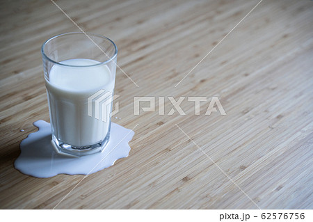 glass on wooden table with milk spilled over in a 62576756